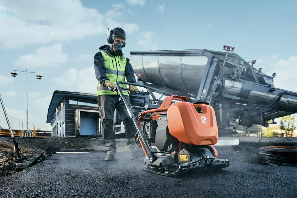 Husqvarna maantiivistäjät käytössä: Mies työskentelee Husqvarna LX 90 maantiivistäjän kanssa asfaltilla, taustalla näkyy rakennustyömaa.