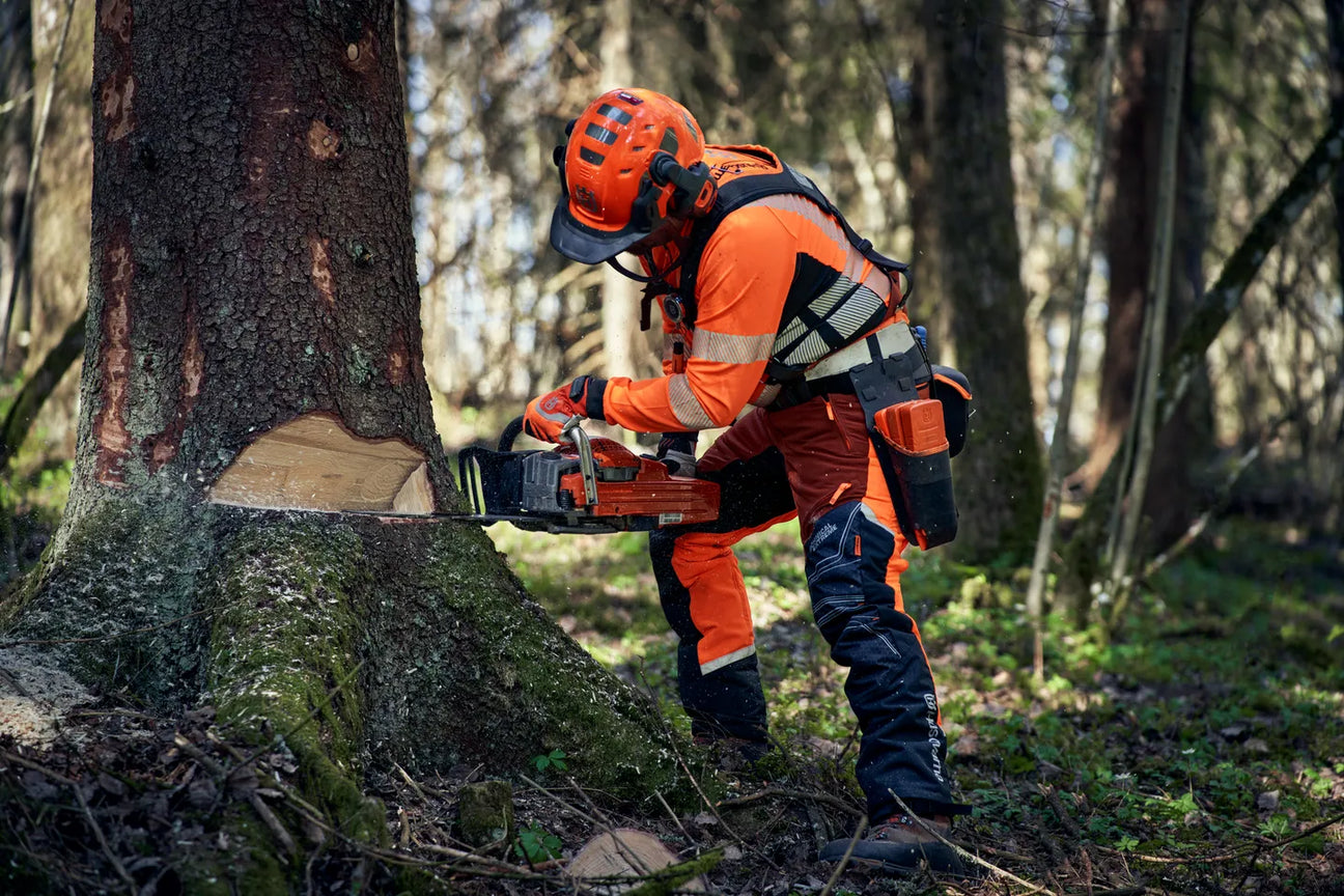 Metsuri työskentelee metsässä Husqvarna suojavarusteet päällään, käyttäen moottorisahaa puun kaatamiseen. Turvallisuus ja mukavuus yhdistyvät Husqvarna suojavarusteissa.
