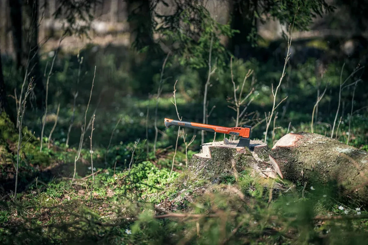 Husqvarna työkalut ja tarvikkeet - Retkikirves kaatuneen puun juurella metsän ympäröimänä, täydellinen valinta metsätyöhön.
